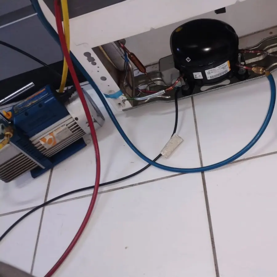 Manifold e bomba de vácuo ligados ao compressor de uma geladeira, durante o conserto na casa do cliente